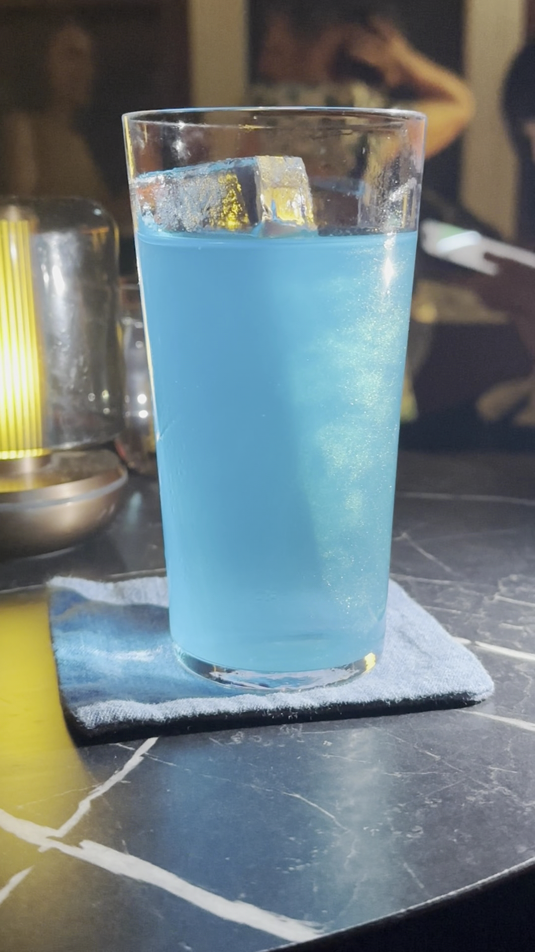 Blue cocktail served on a blue fabric coaster